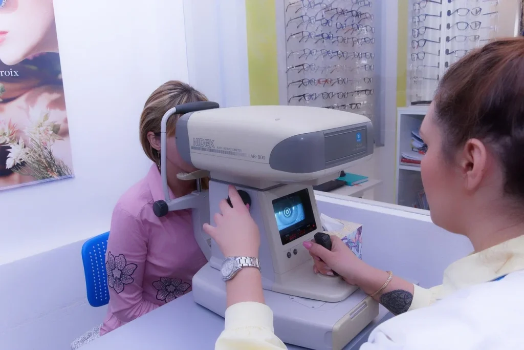 A woman is seated at an eye exam machine, adjusting her position for a vision test.